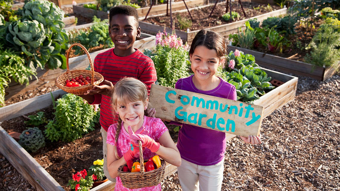 Kids in a community garden holding the fruits and vegetables that they have grown.