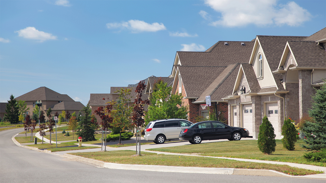 There is a street with homes side by side and some green space between the homes.