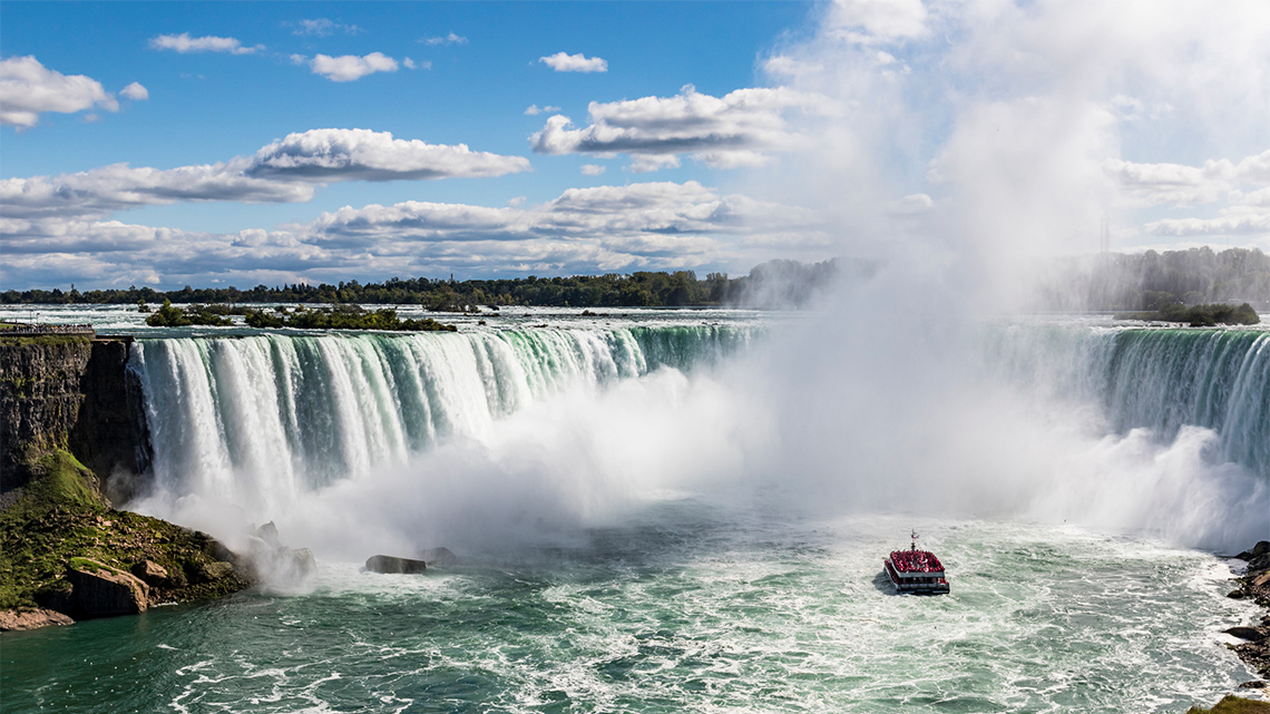 This is an image of Niagara Falls. There is water coming down with a thick mist in front. There is also a small boat riding towards the mist.