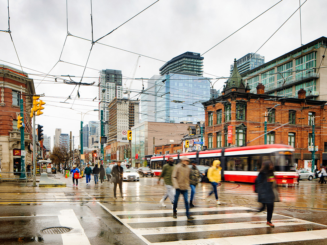 A streetcar on a busy route in downtown Toronto. There are people crossing the street.