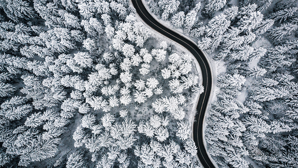 Aerial view of a road in a forest covered in snow. 