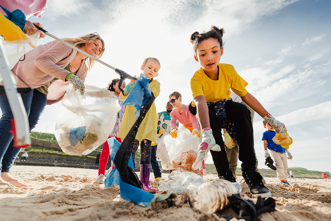 A group of young students pick up litter on a beach.