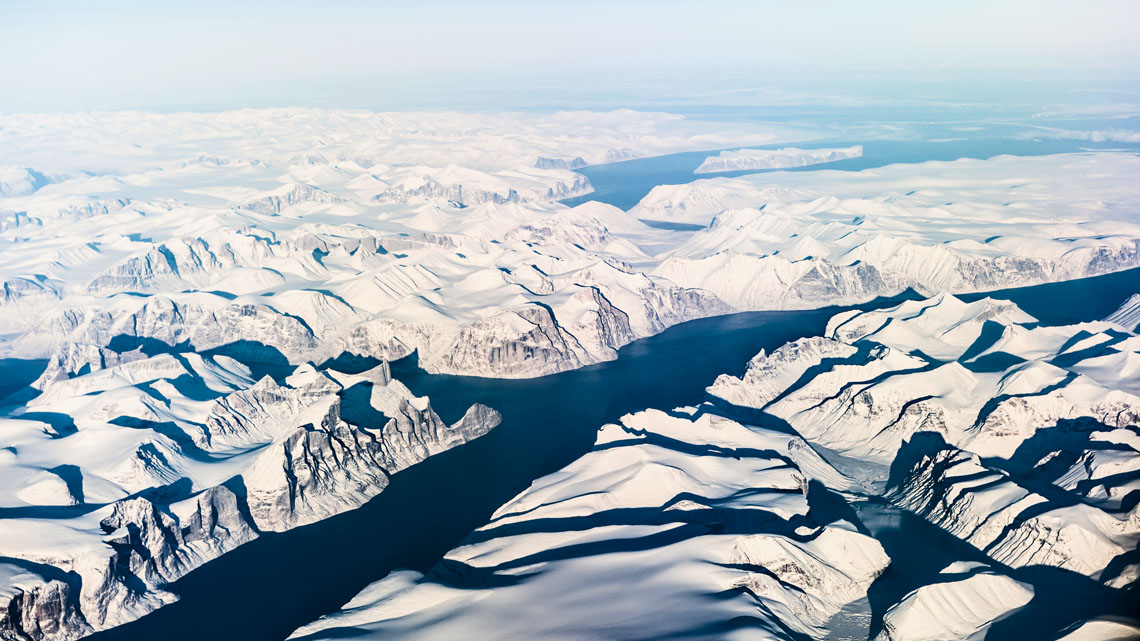 A large river flowing through a rocky landscape covered in snow with a coast in the background.