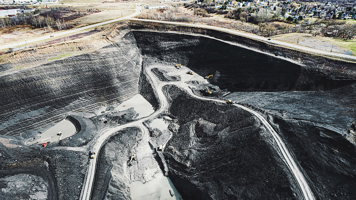 Aerial view of machines working in a large open pit mine. There is a neighbourhood next to the mine.