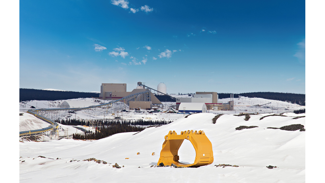 A large iron processing plant in a rocky landscape covered in snow with forests in the background.