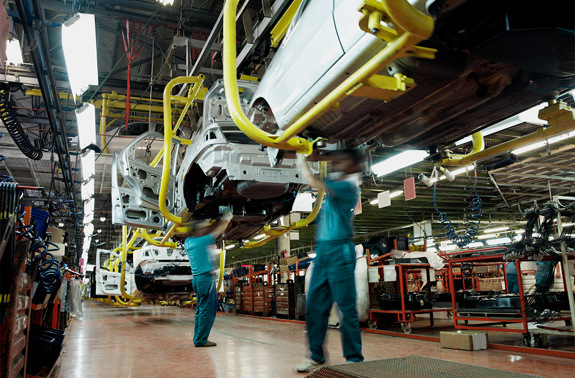 Workers build cars on an assembly line in a factory.
