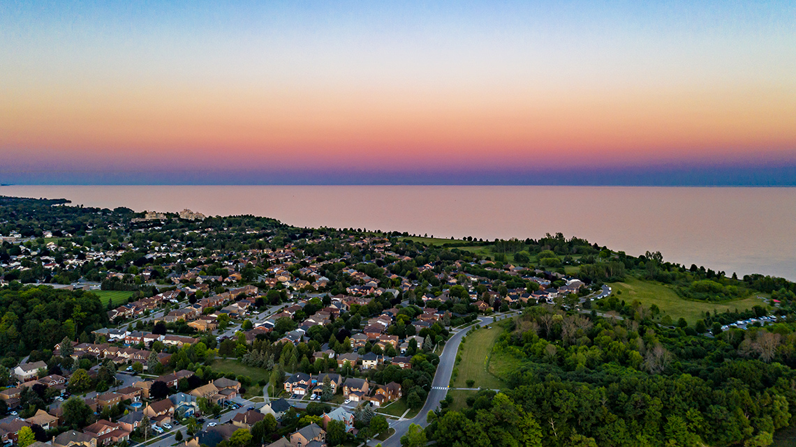 A neighbourhood of houses next to a lake that extends to the horizon in the background.