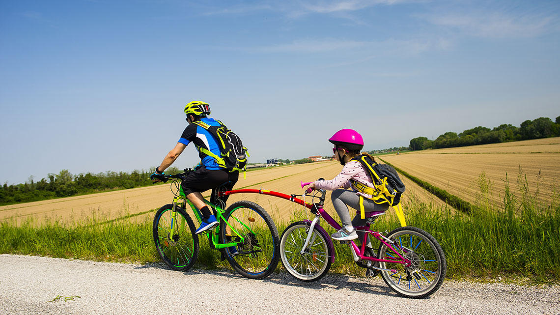 Two mountain bikers ride on a trail with a forest and mountains in the background.