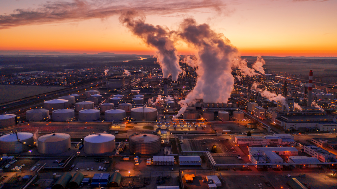 A Large factory with smoke rising out of multiple chimneys.