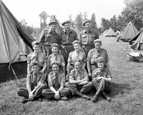 There are eleven members of the Royal Canadian Army Medical Corps smiling for the photo. They are outside with trees and tents in the background.